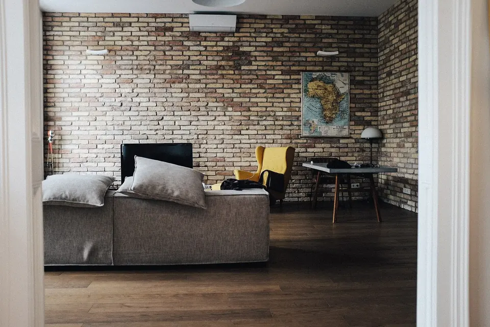 A living room with an exposed brick wall, a grey sofa and a flat-screen TV on a low unit