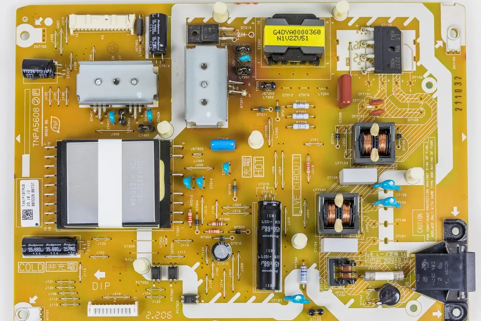 A yellow TV power supply board with printed part numbers and a barcode sticker beside the transformers